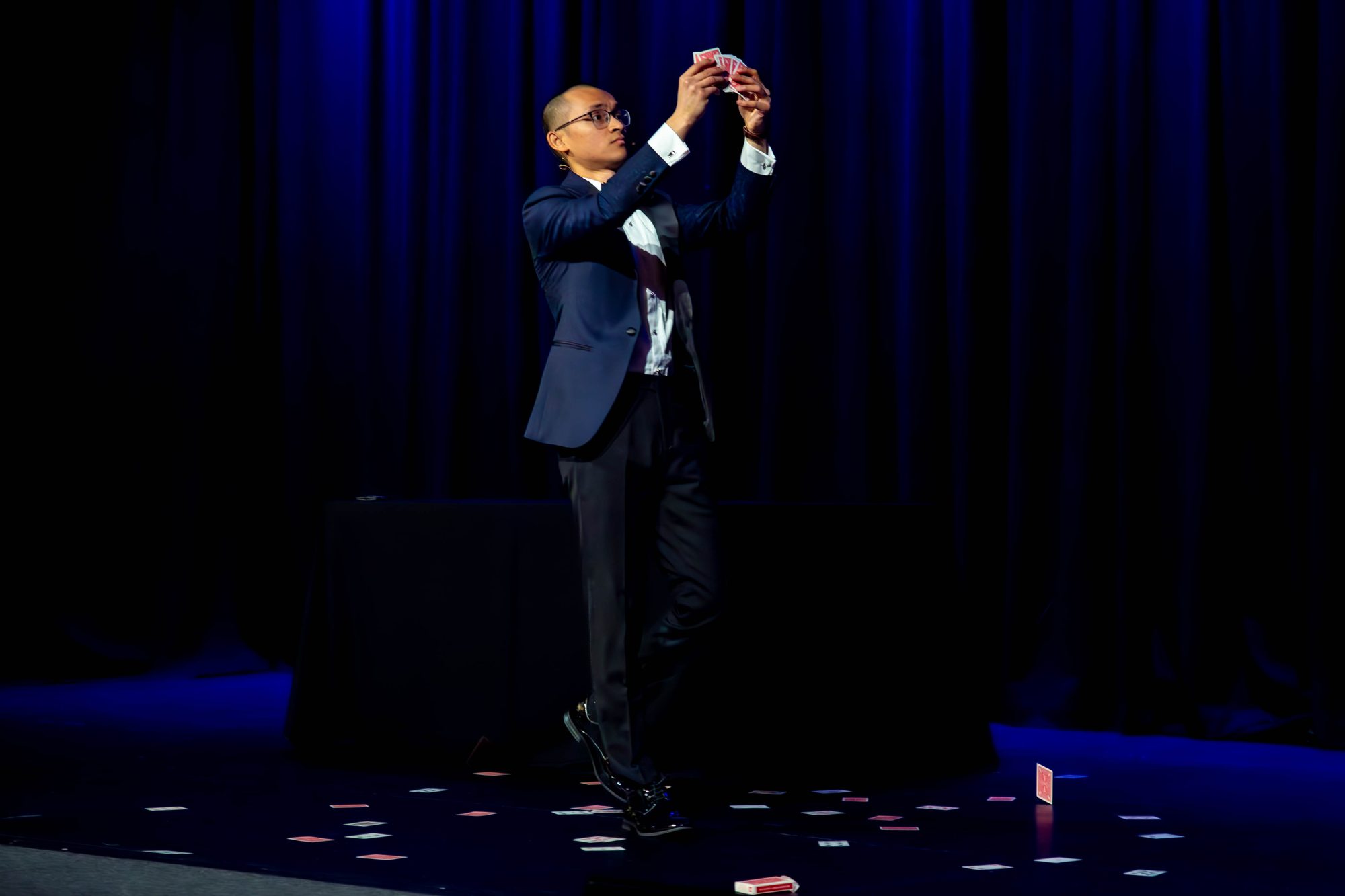 Baenedict on stage at a university ball, cards frozen mid-air